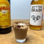 closeup of peanut butter cup shot on a wooden table with kahlua and peanut butter whiskey next to the glass