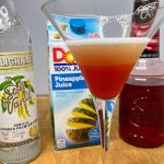 pineapple upside down cake martini with ingredient bottles next to the glass