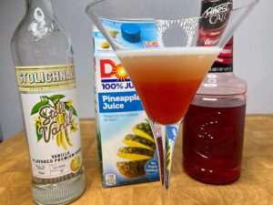 pineapple upside down cake martini with ingredient bottles next to the glass