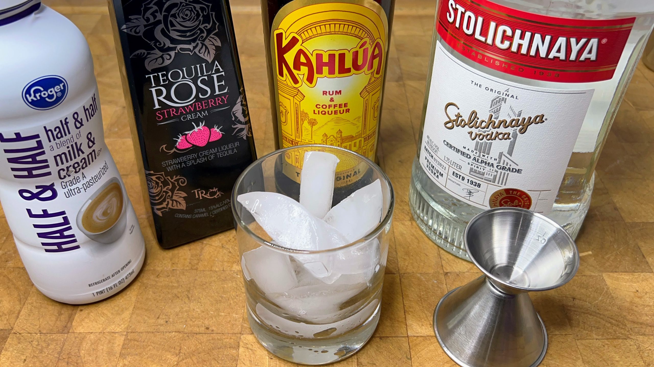 rocks glass filled with ice next to a jigger, vodka, kahlua, tequila rose and half and half