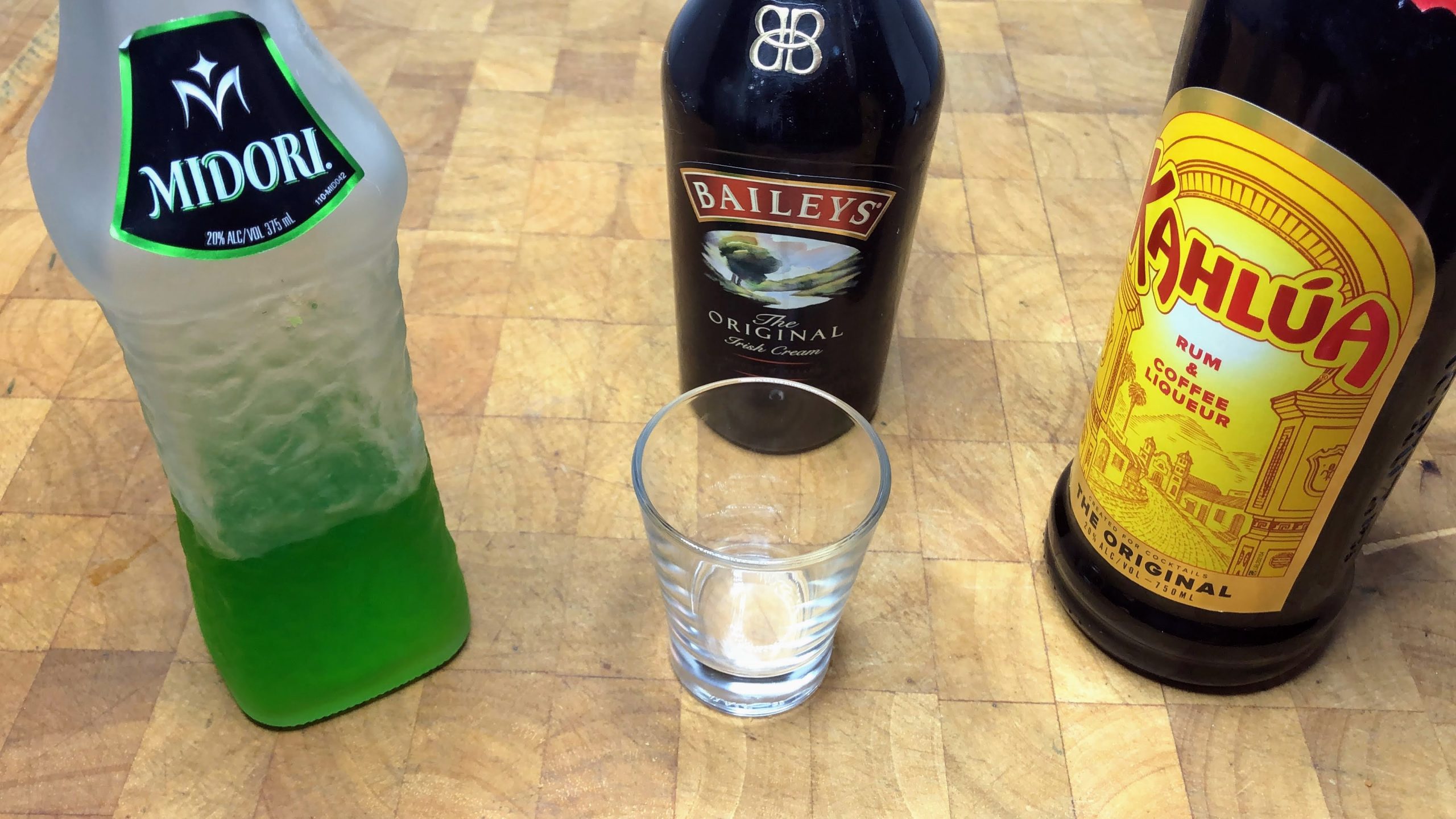 empty shot glass next to bottle of midori, irish cream and kahlua