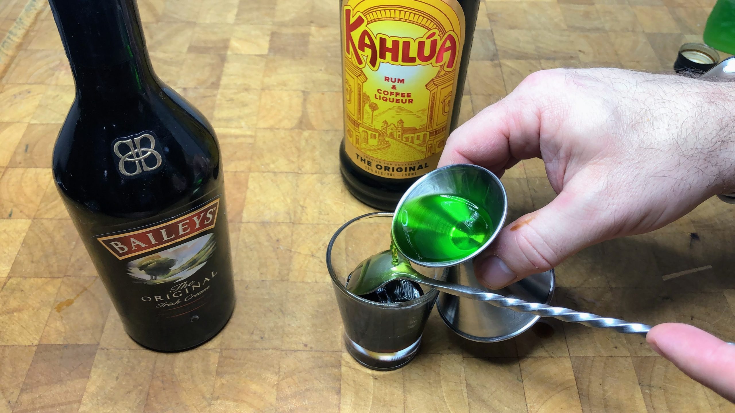 pouring midori over the back of a bar spoon into shot glass