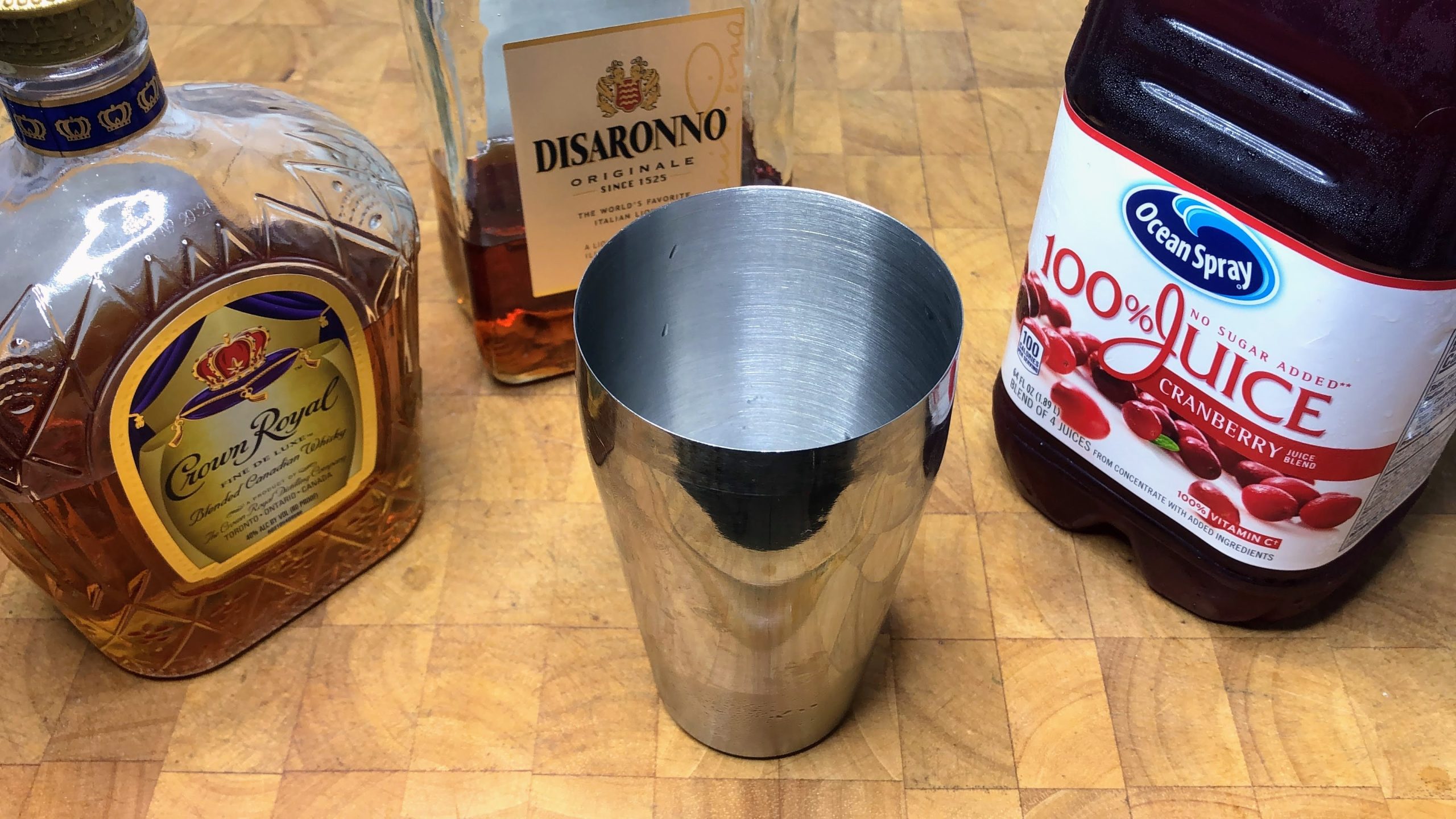 cocktailo shaker next to bottles of amaretto, crown royal and cranberry juice