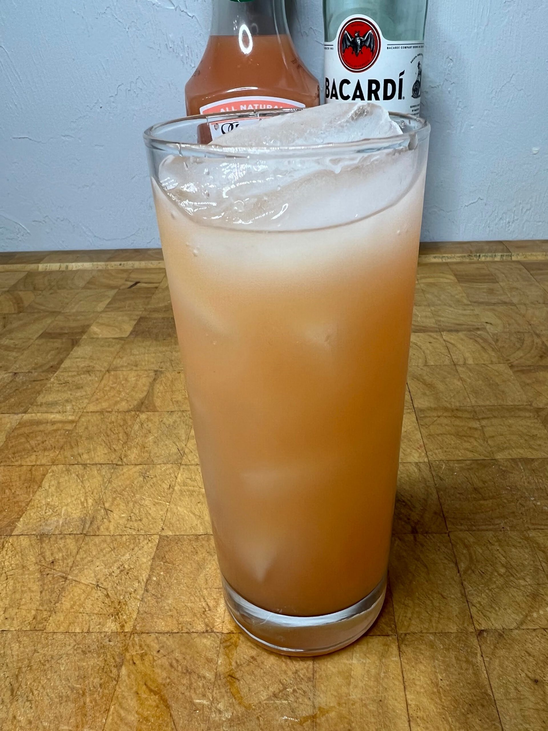 closeup of rum and grapefruit juice in a highball glass on a wooden table with ingredient bottles in the background