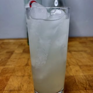 rum and limeade in a highball glass on a wooden table with ingredients in the background
