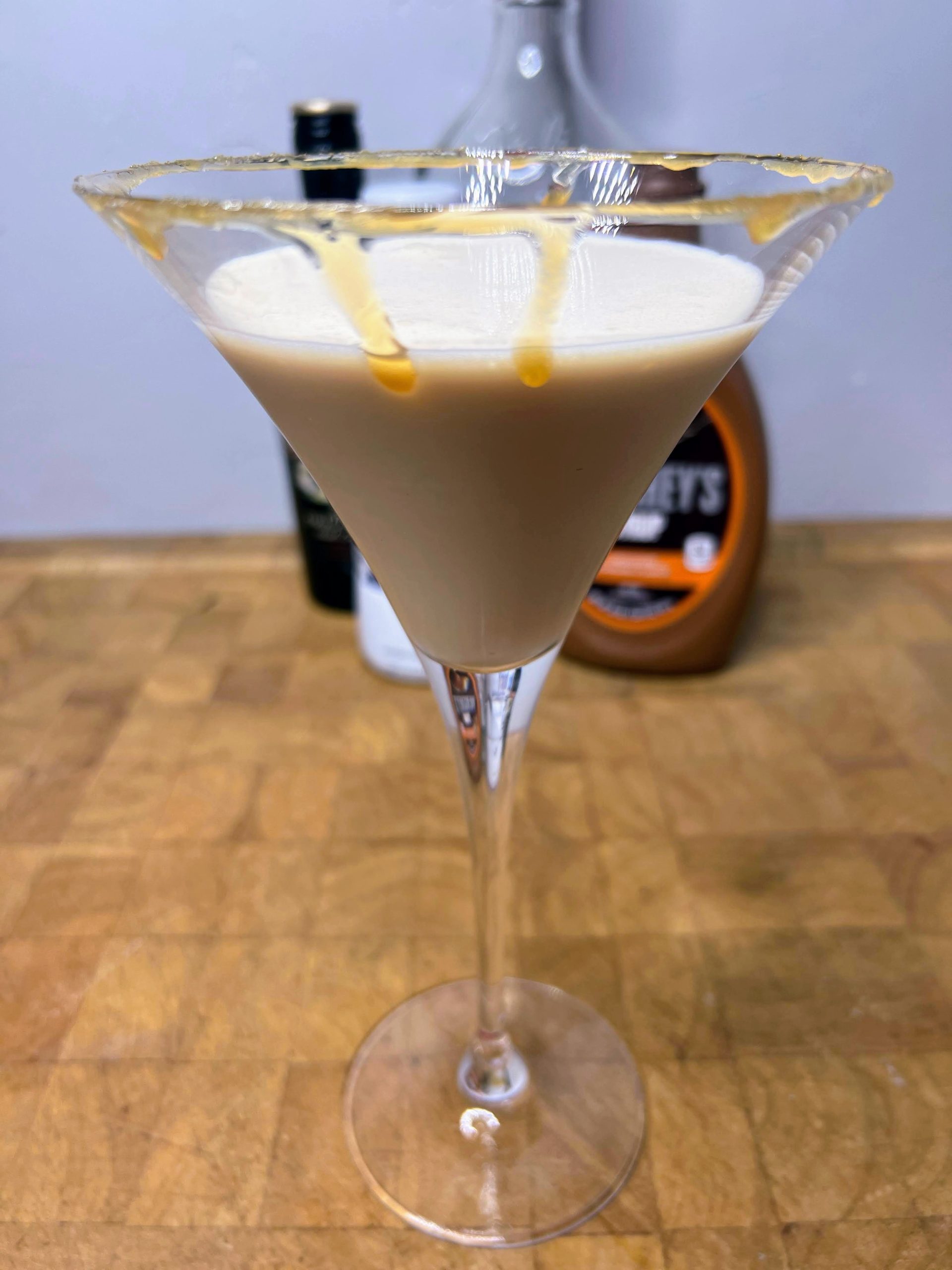 closeup of salted caramel martini on a wooden table with ingredient bottles in the background