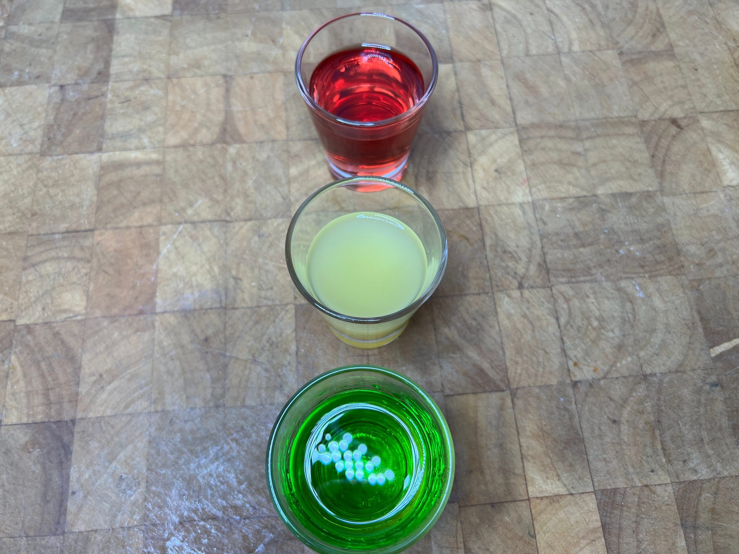 stop light shots: three shot glass with red, yellow and green colored shots on a wooden tabled