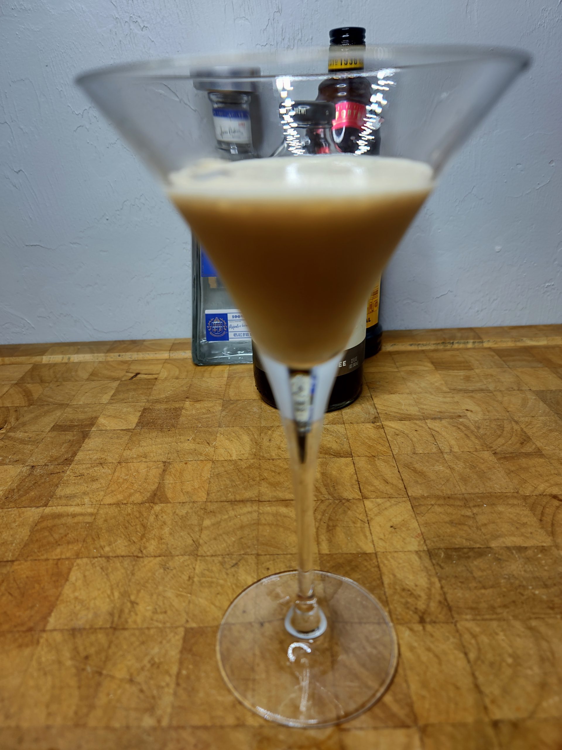 closeup of tequila espresso martini on a wooden table with ingredient bottles in the background