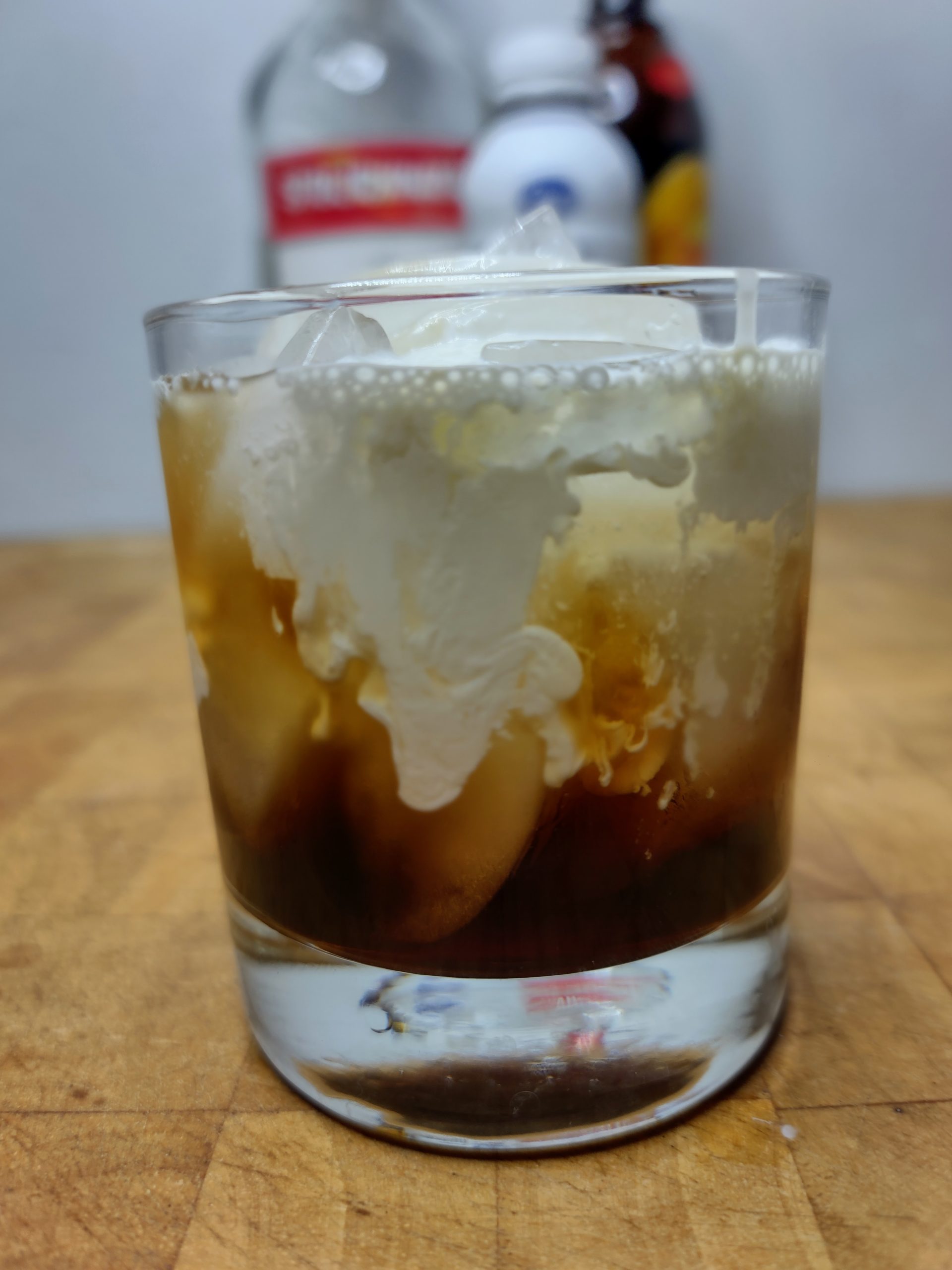 closeup of white russian cocktail with ingredients behind the glass