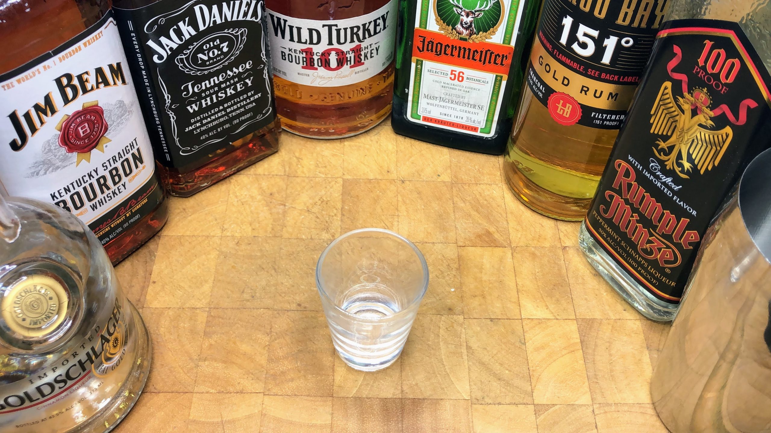 empty shot glass next to bottles of goldschlager, jim beam, jack daniels, wild turkey, jager, 151, and rumpleminze