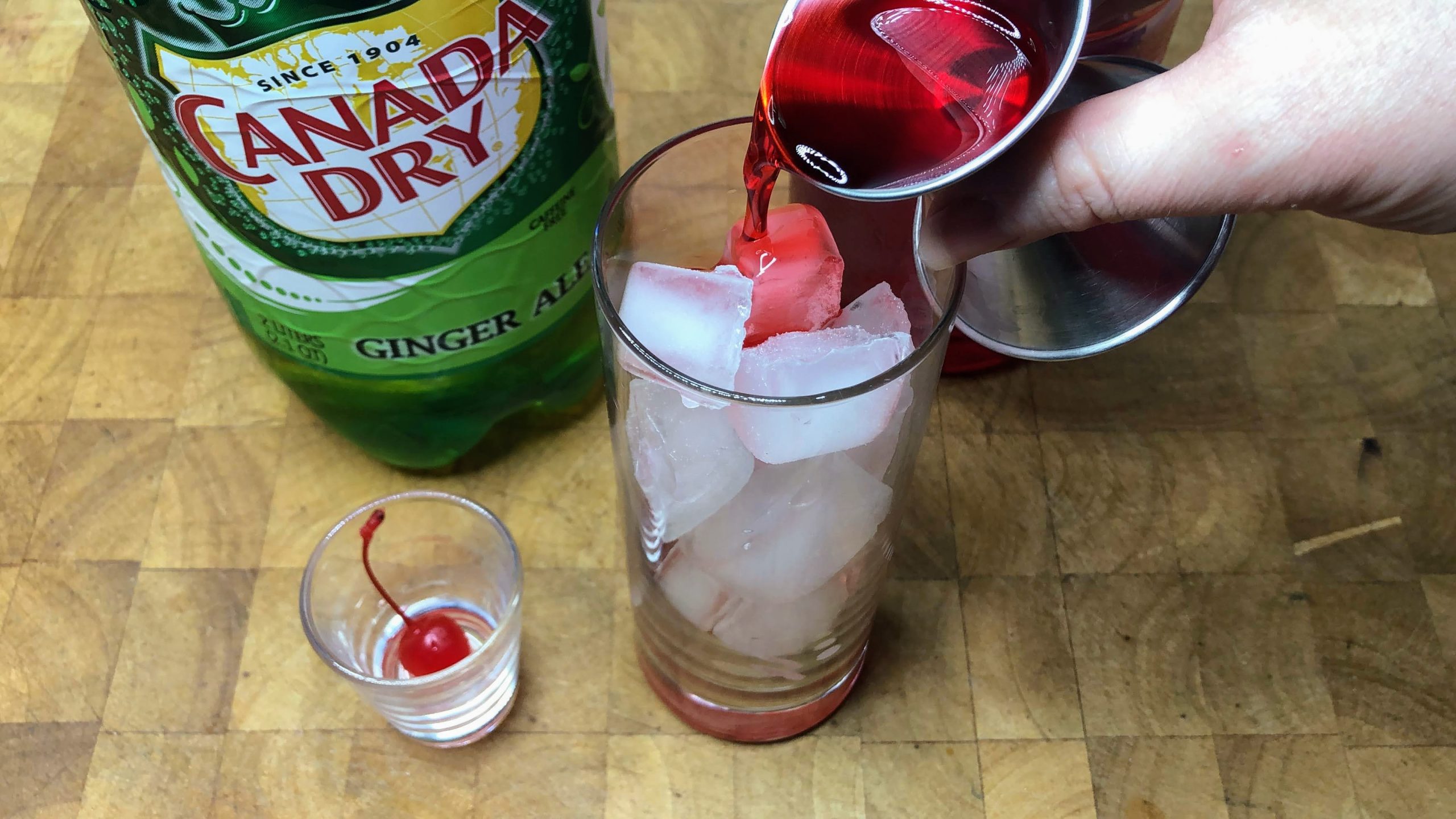 Pouring grenadine from a jigger into a highball glass.