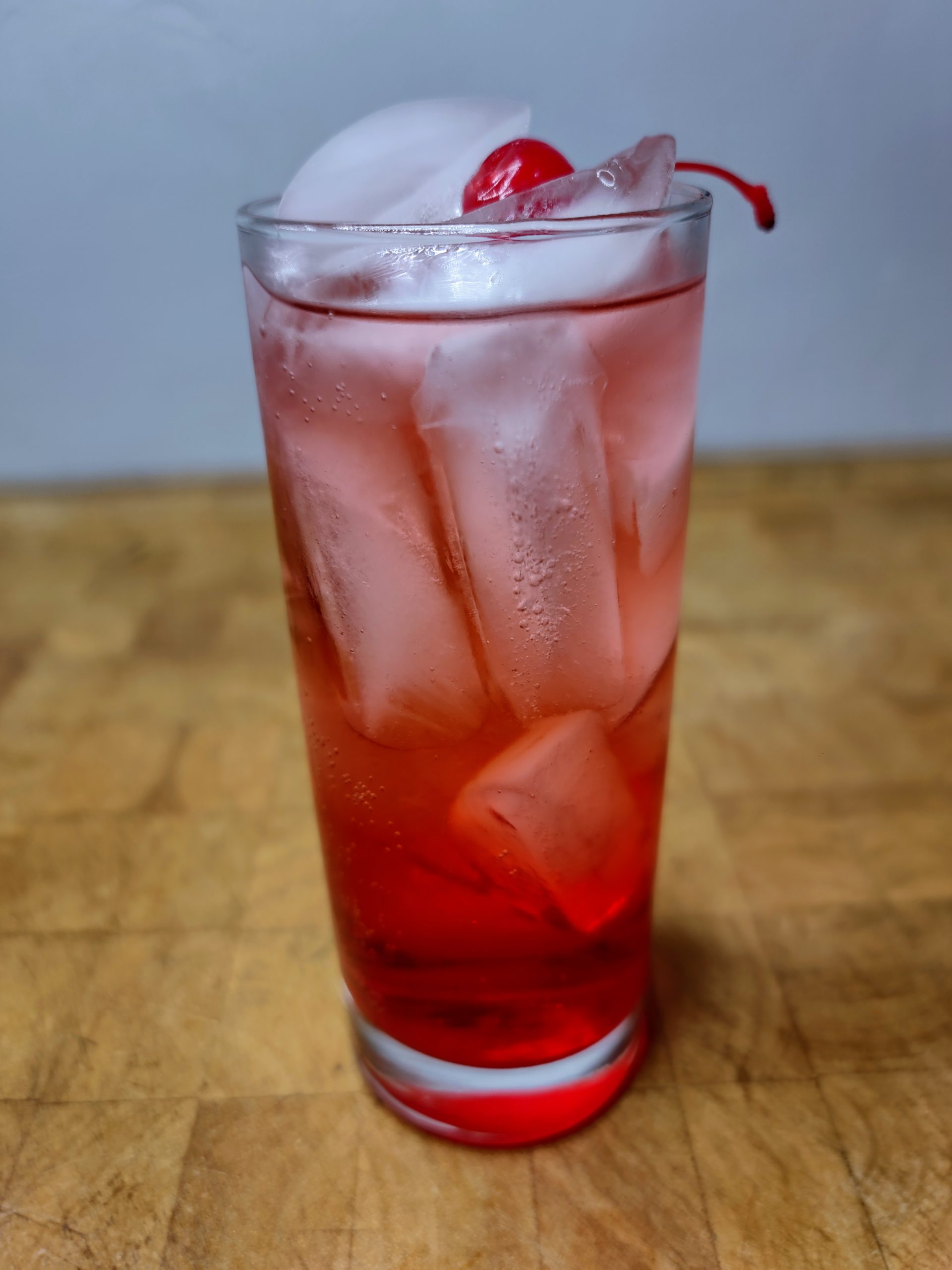 Shirley temple drink in a highball glass topped with a cherry.