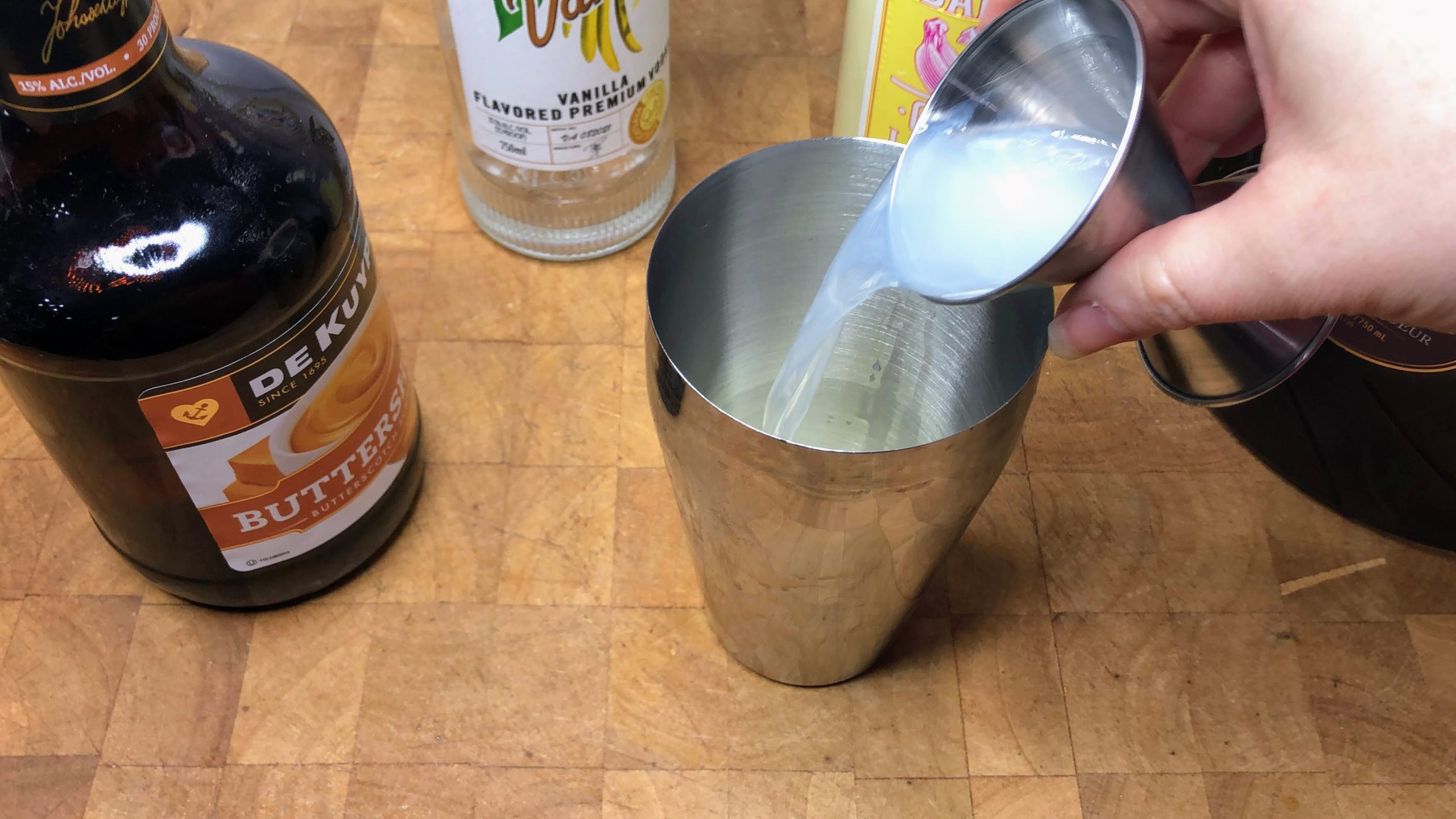 Pouring vanilla vodka from a jigger into a shaker.