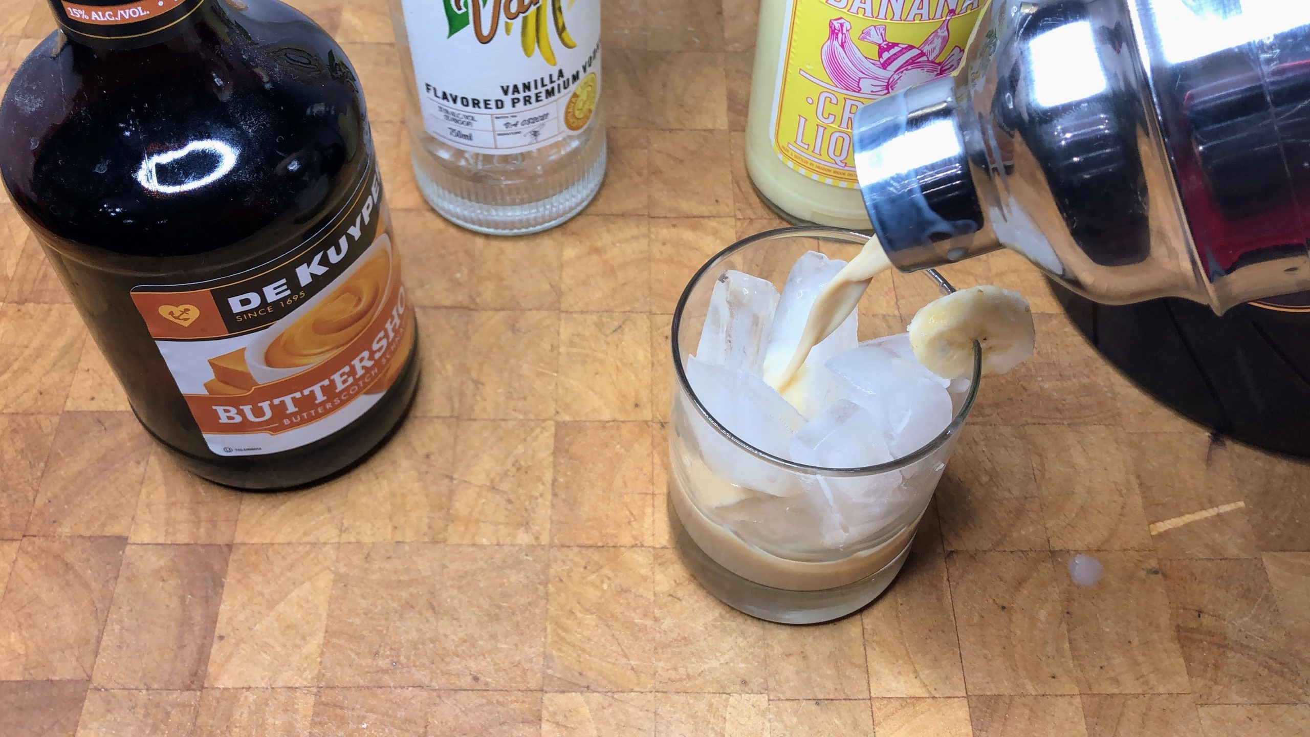 Pouring banana foster drink from shaker into a glass.
