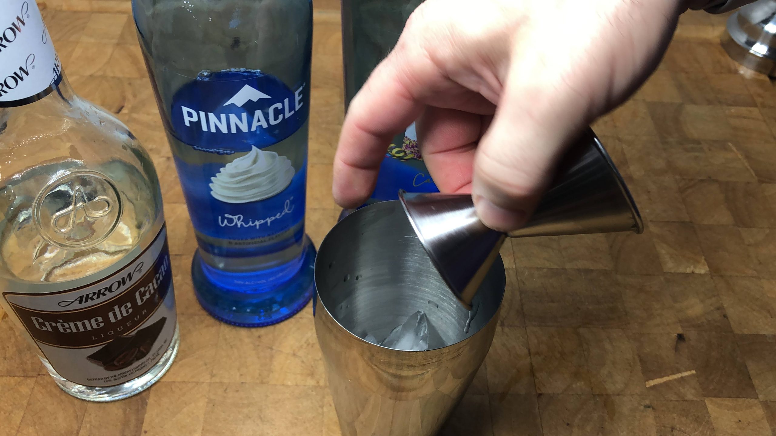 Pouring whipped cream vodka from a jigger into a shaker.