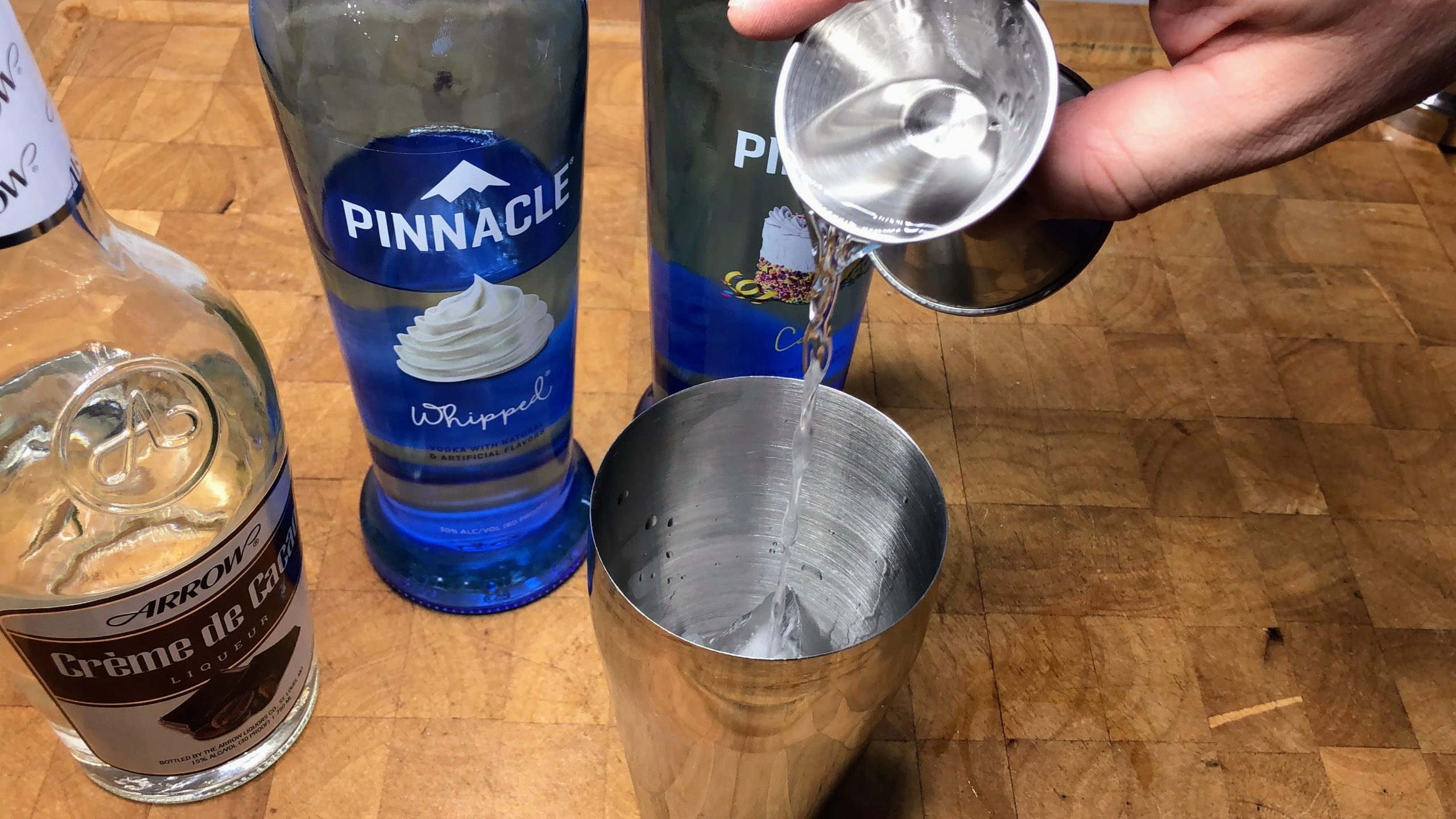 Pouring creme de cacao from a jigger into a shaker.