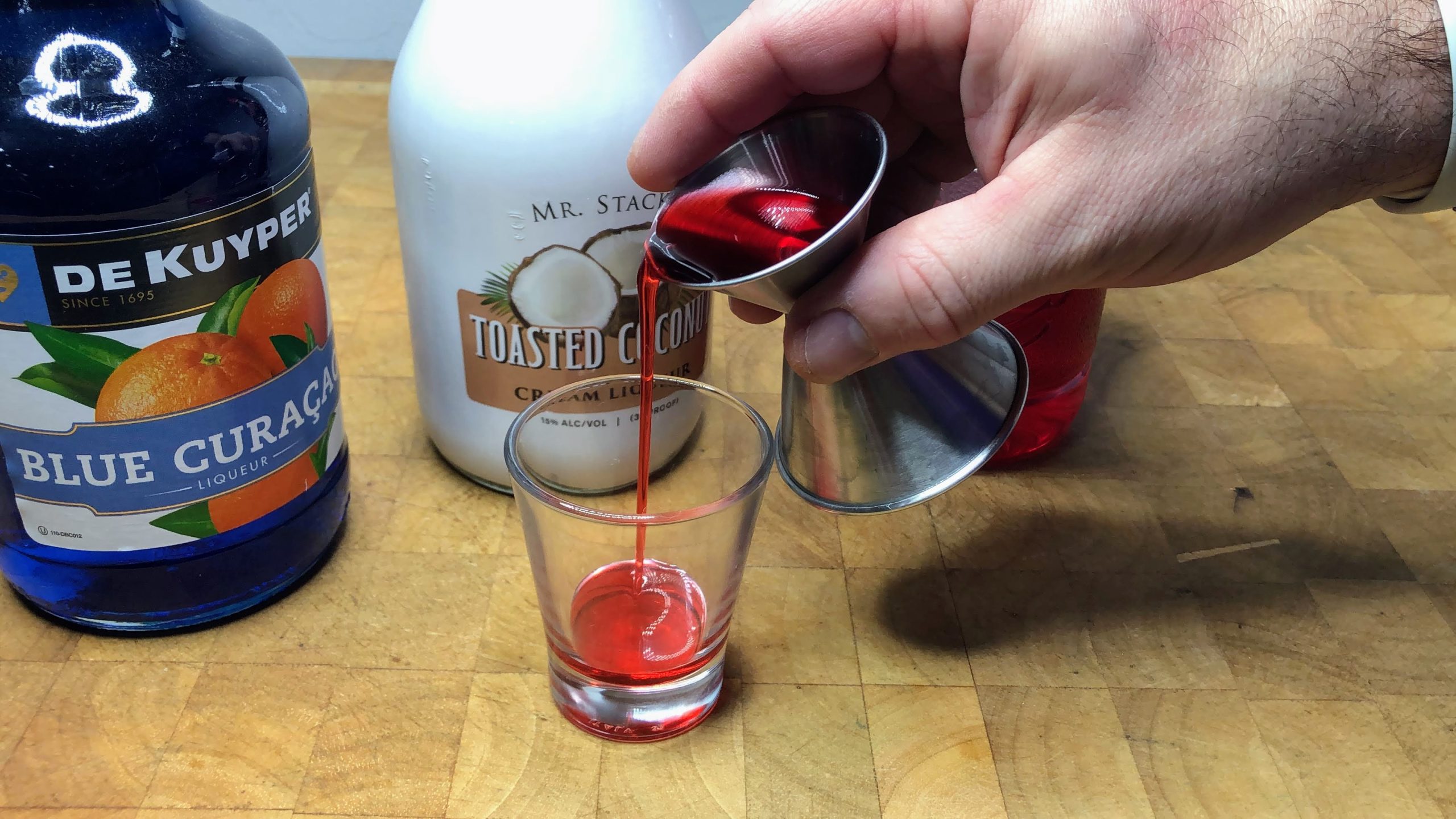 Pouring grenadine into a shot glass.
