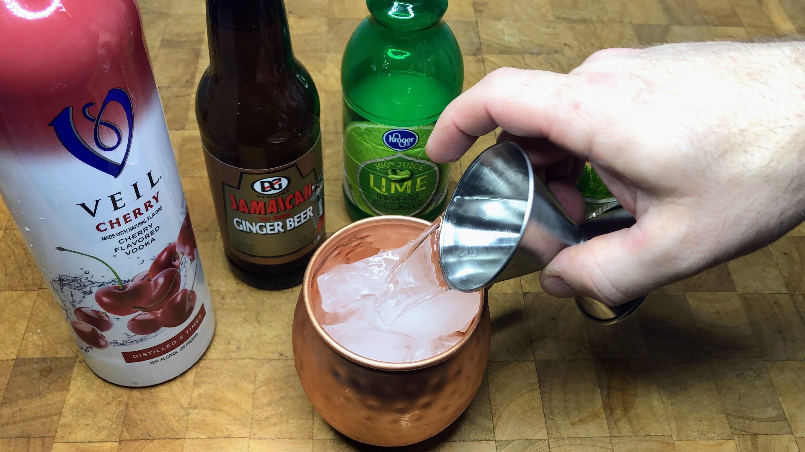 Pouring cherry vodka from a jigger into a copper mug.