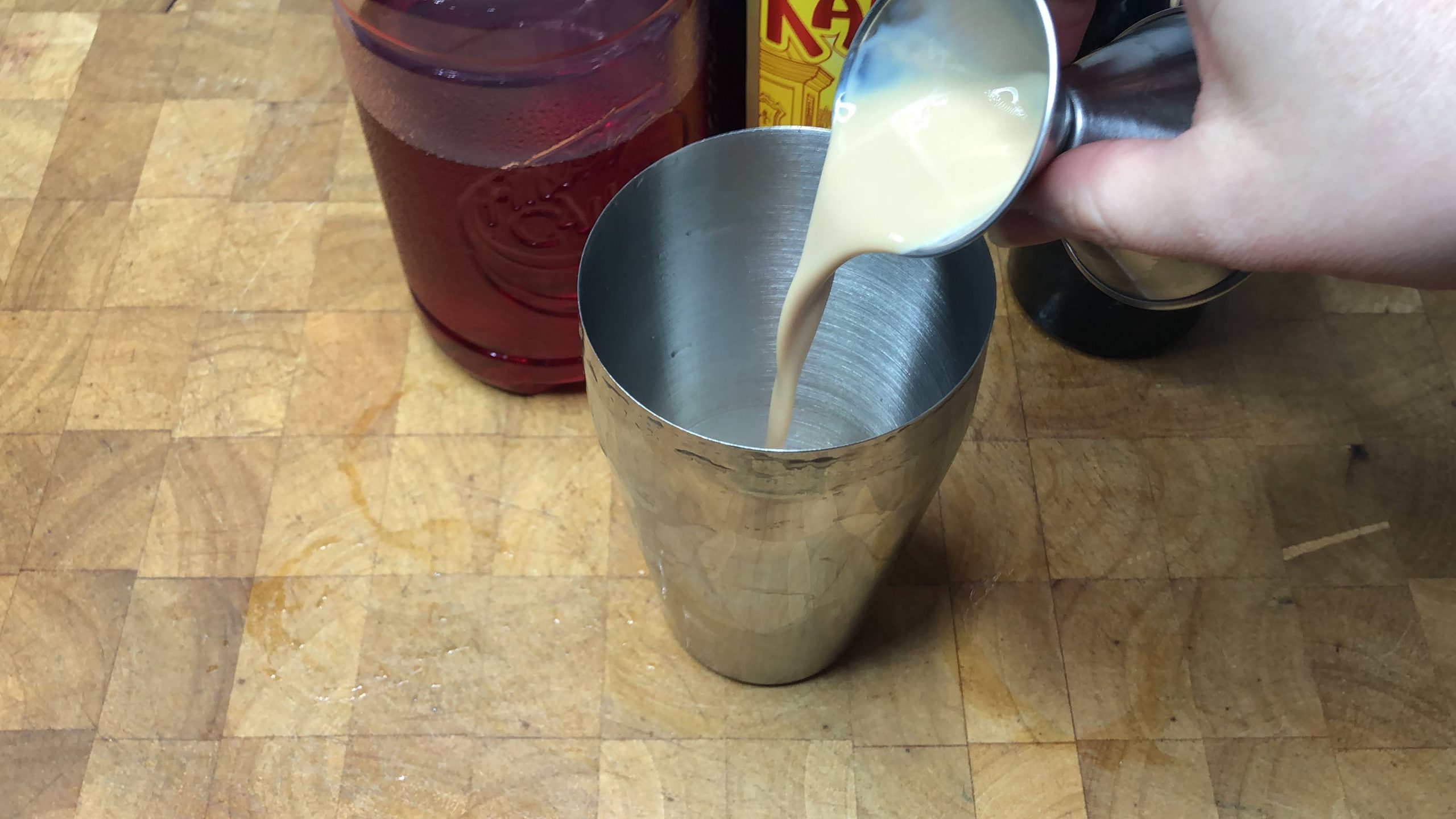 Pouring irish cream from a jigger into a cocktail shaker.