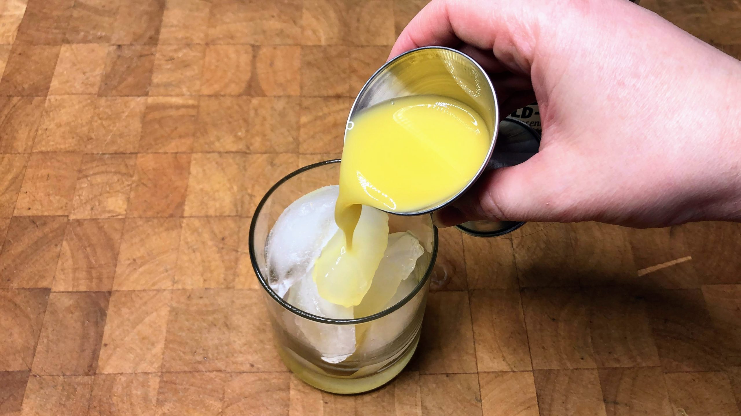 Pouring orange juice from a jigger into a rocks glass.