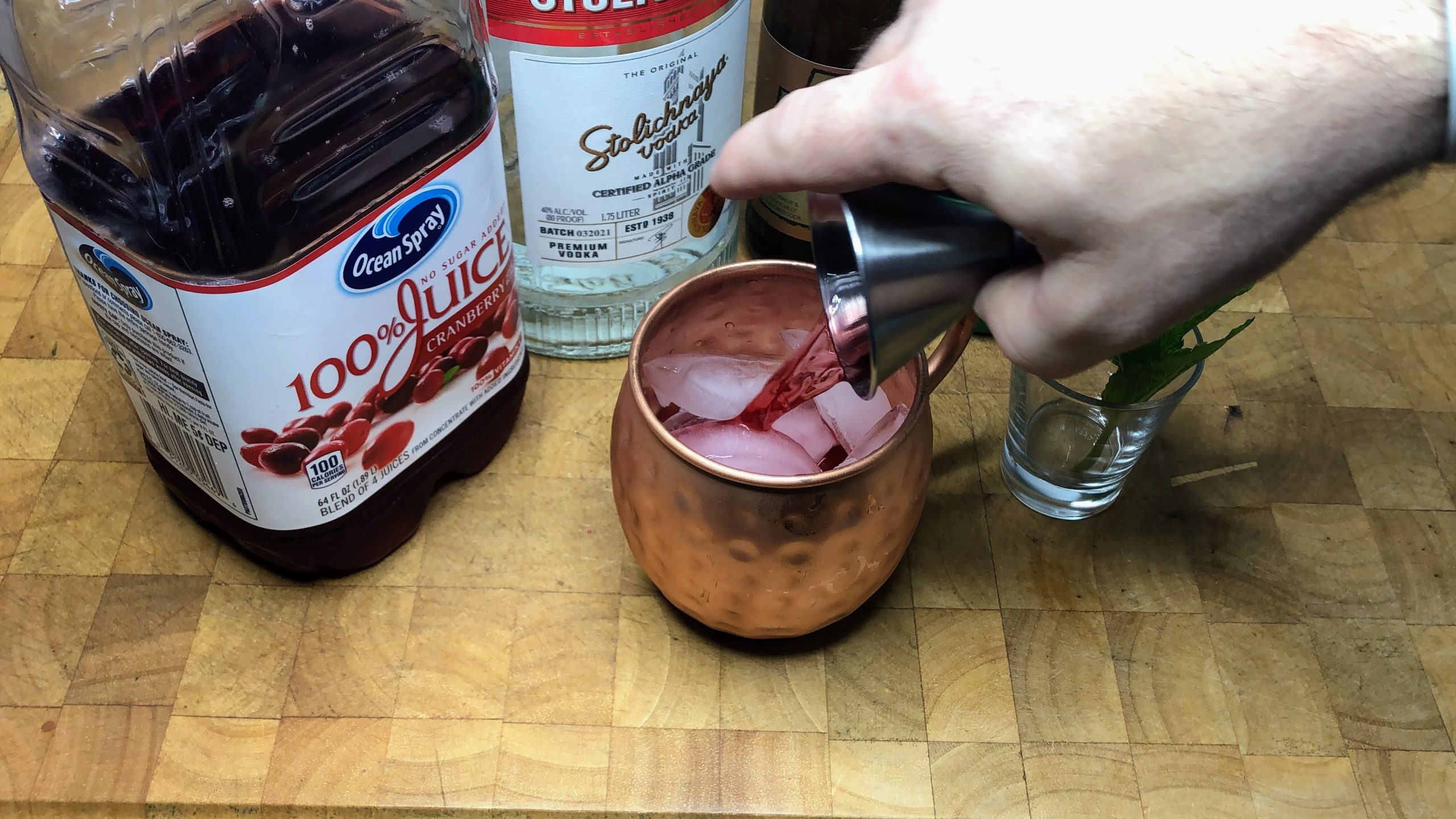 Pouring cranberry juice from a jigger into a copper mug.