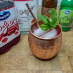 Cranberry moscow mule with a sprig of mint next to the ingredient bottles.