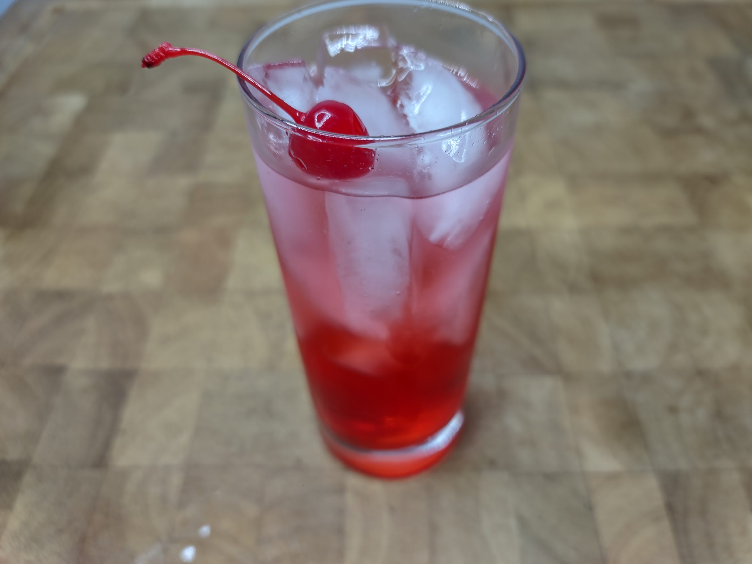 Dirty shirley cocktail in a highball glass with cherry garnish.