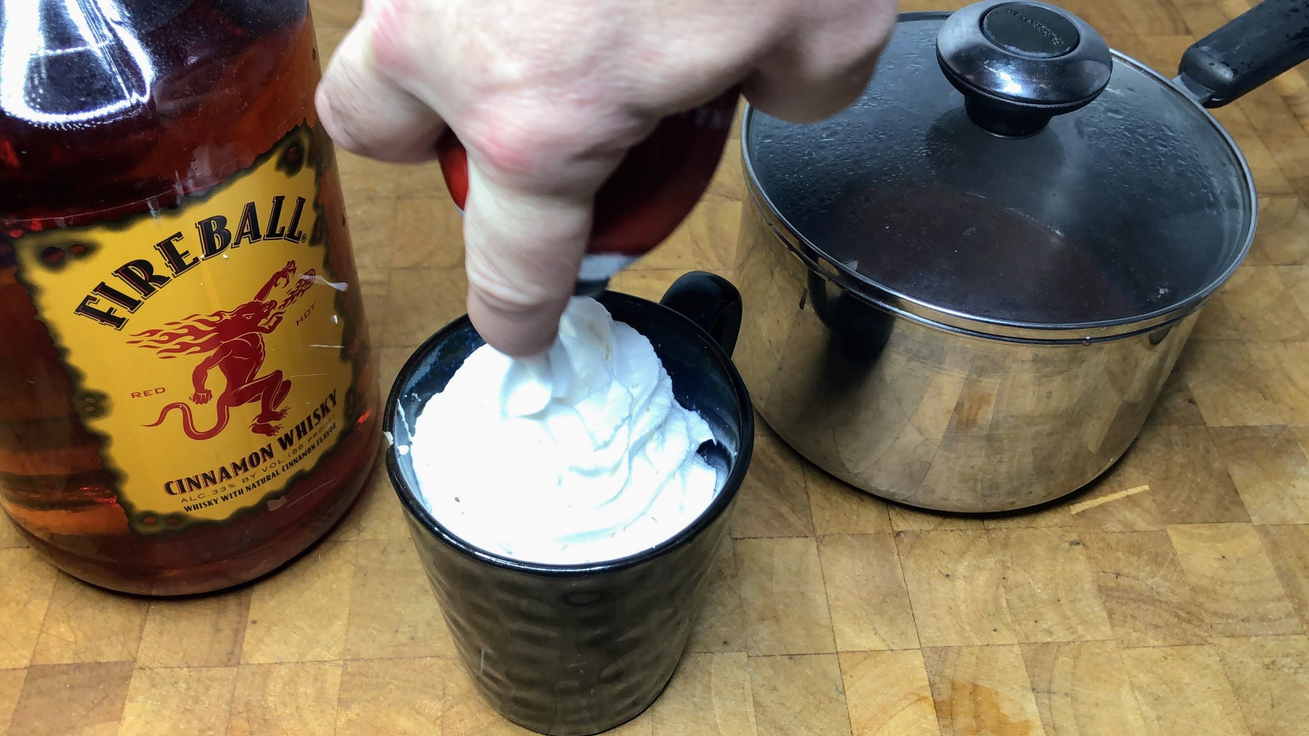 Adding whipped cream on top of fireball hot chocolate.