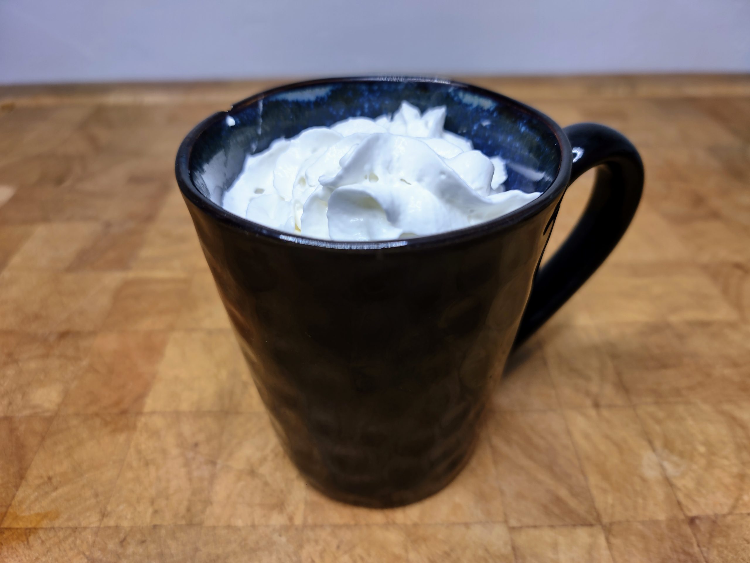 fireball hot chocolate in a blue mug topped with whipped cream on a wooden table