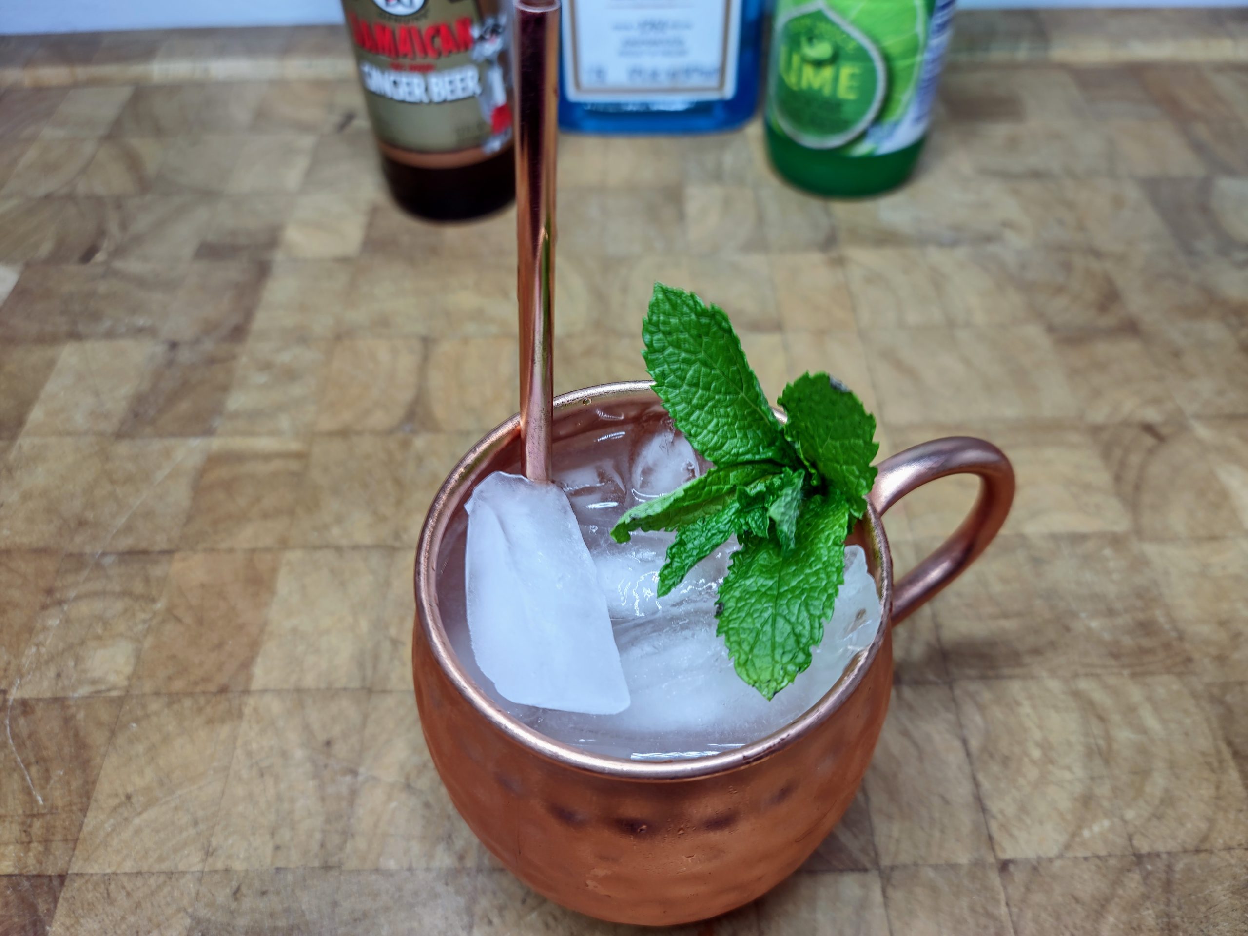 gin-gin mule in a copper mug with mint and a copper straw.  Ingredient bottles in the background.