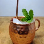 gin-gin mule in a copper mug with mint and a copper straw on a wooden table.