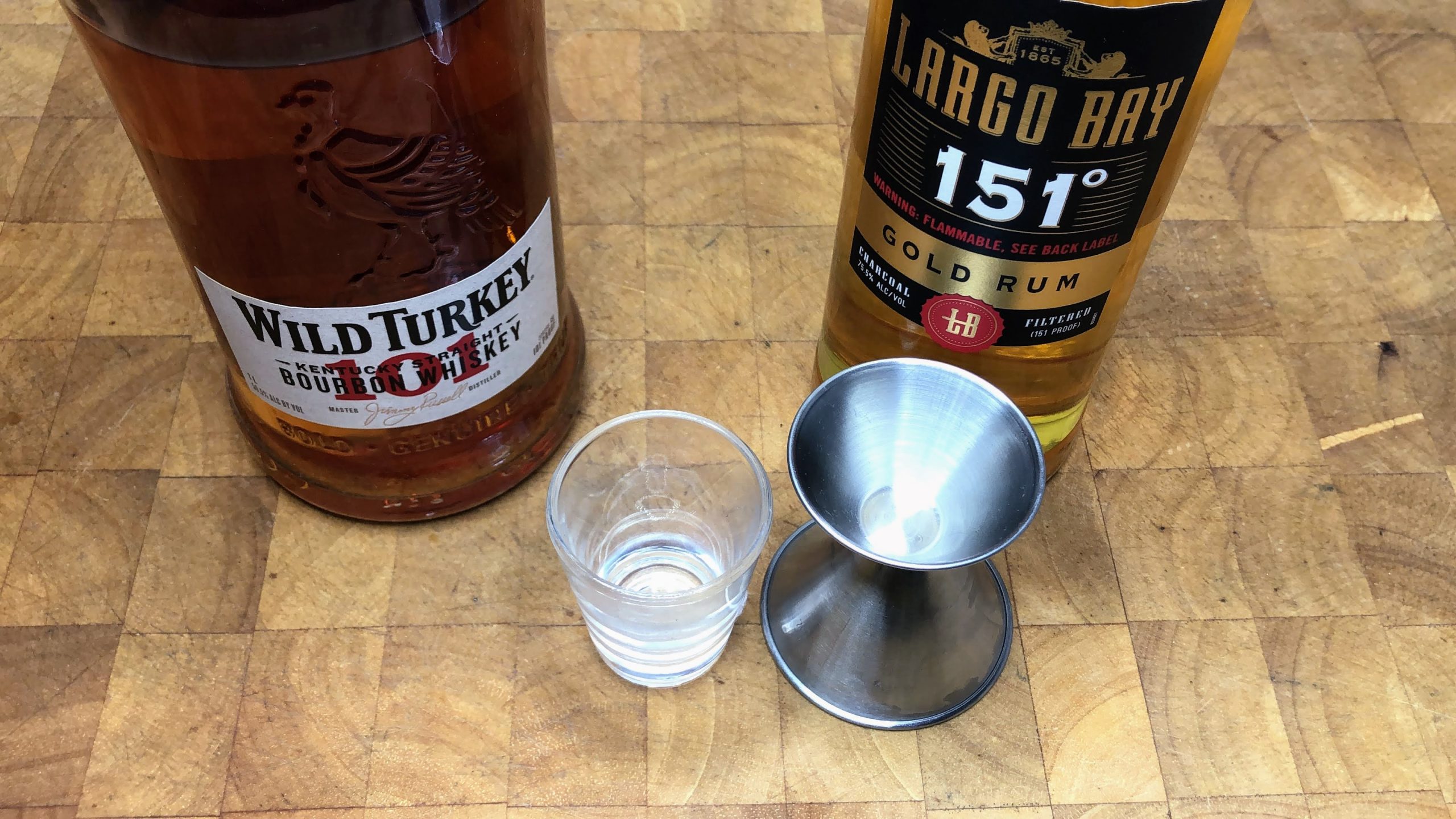 Empty shot glass next to a jigger, 151 rum and wild turkey.