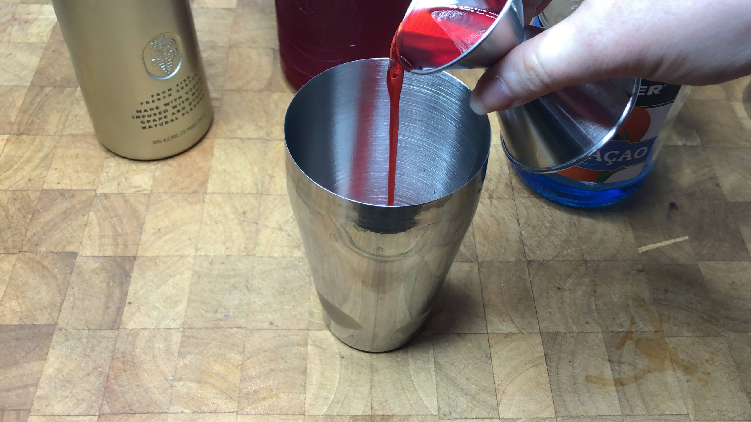 Pouring grenadine from a jigger into a shaker.