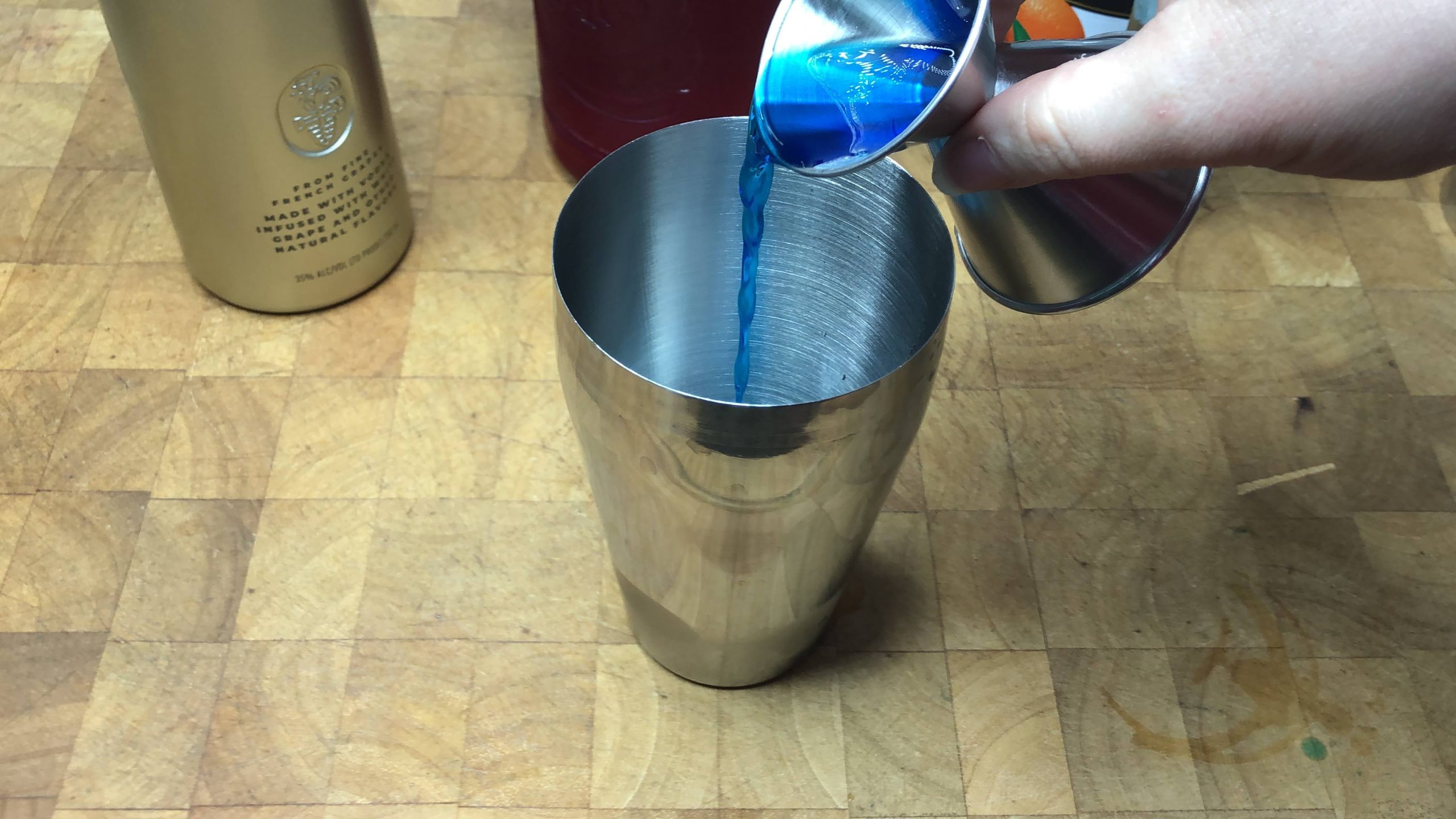 Pouring blue curacao from a jigger into a shaker.