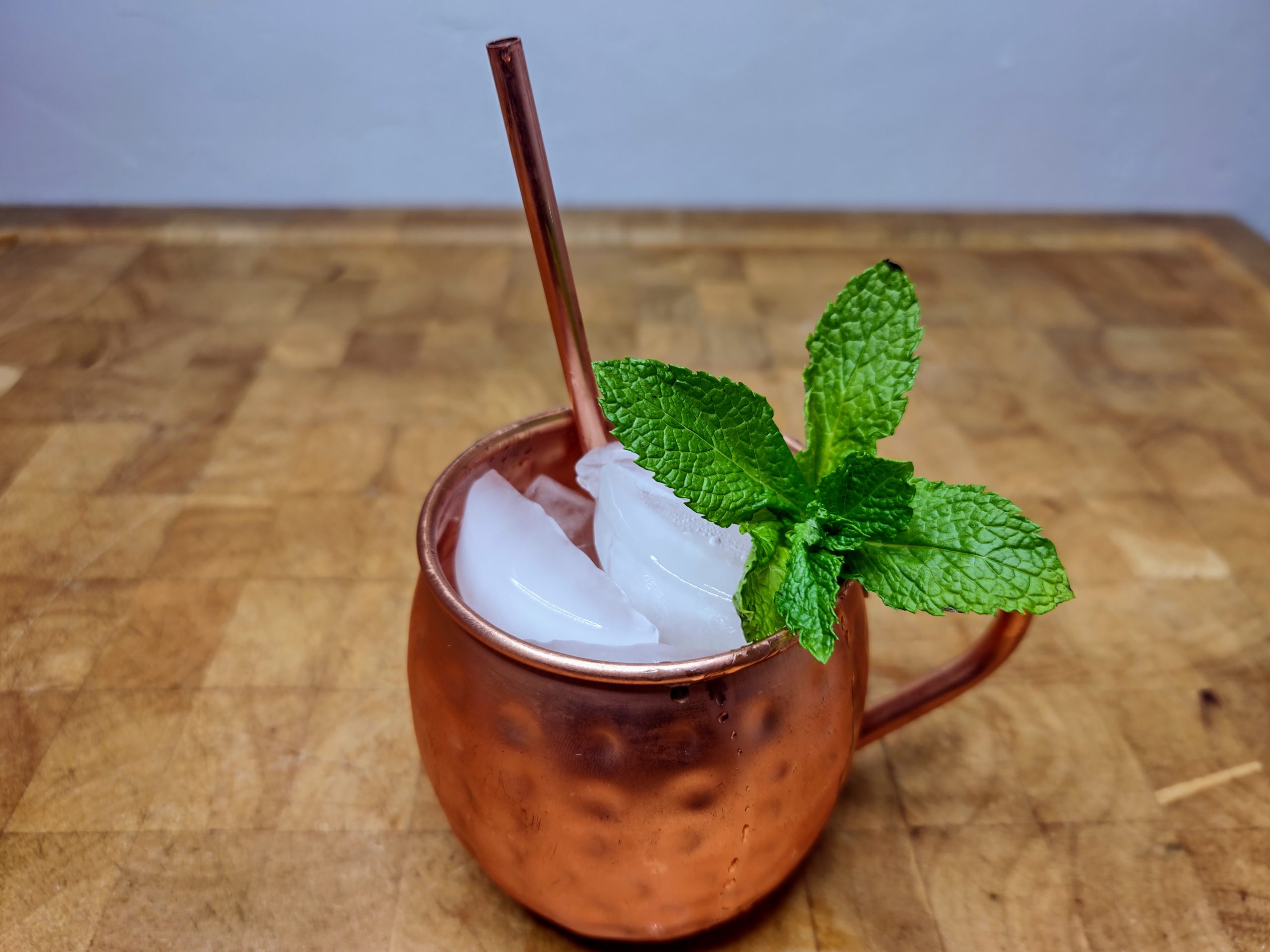 Grape moscow mule with a sprig of mint and copper straw on a wooden table.