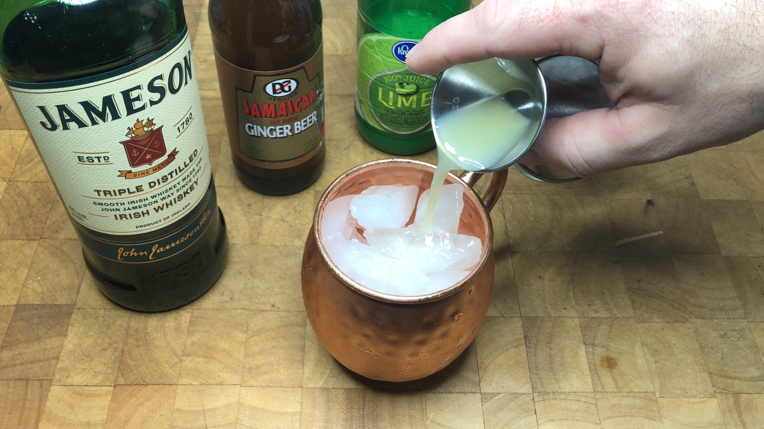 pouring lime juice from jigger into copper mug.