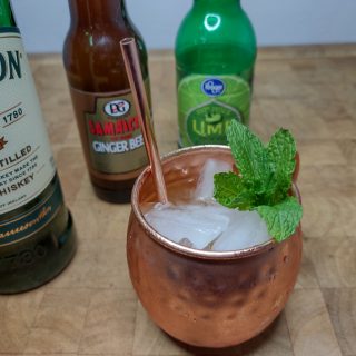 Irish Mule in a copper mug with a copper straw and sprig of mint; ingredient bottles are next to the mug.