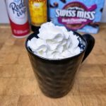 Kahlua hot chocolate topped with whipped cream with ingredients behind the mug.