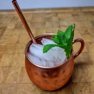 closeup of mexican mule in a copper mug with a copper straw and a sprig of mint on a wooden table