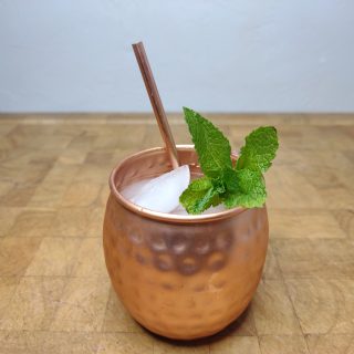 moscow mule in a copper mug with a copper straw and mint on a wooden table.