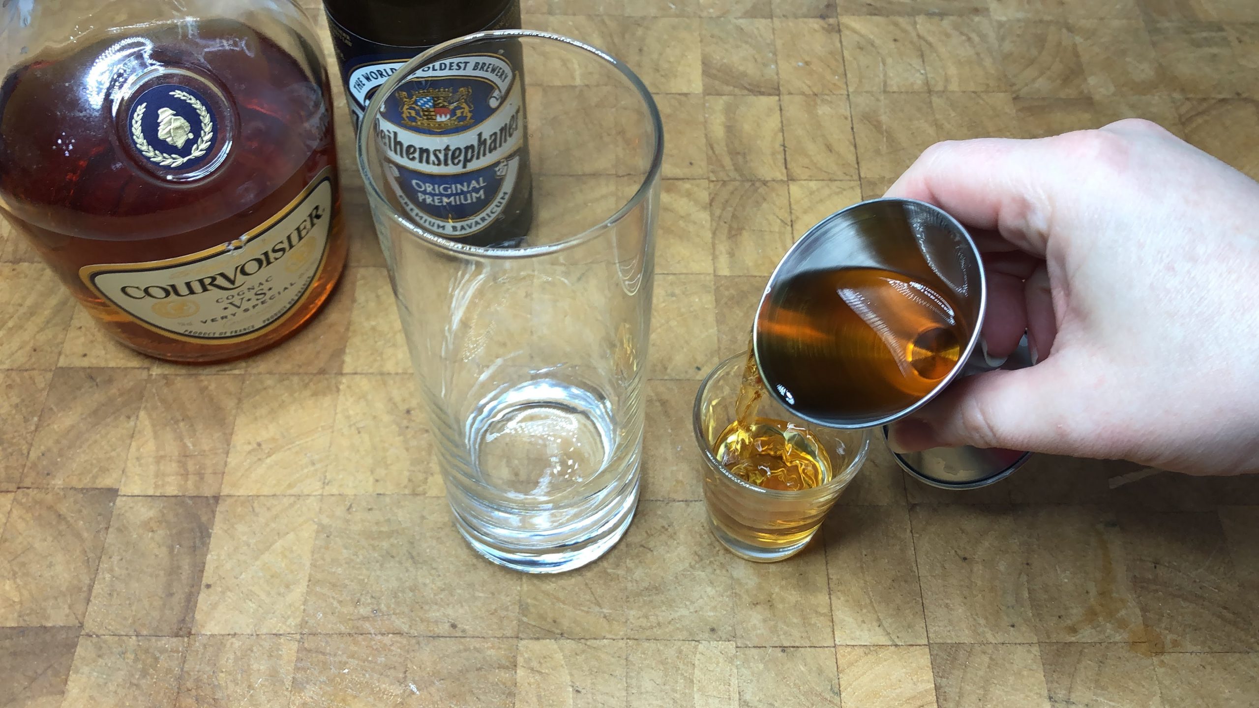 Pouring cognac from a jigger into a shot glass.
