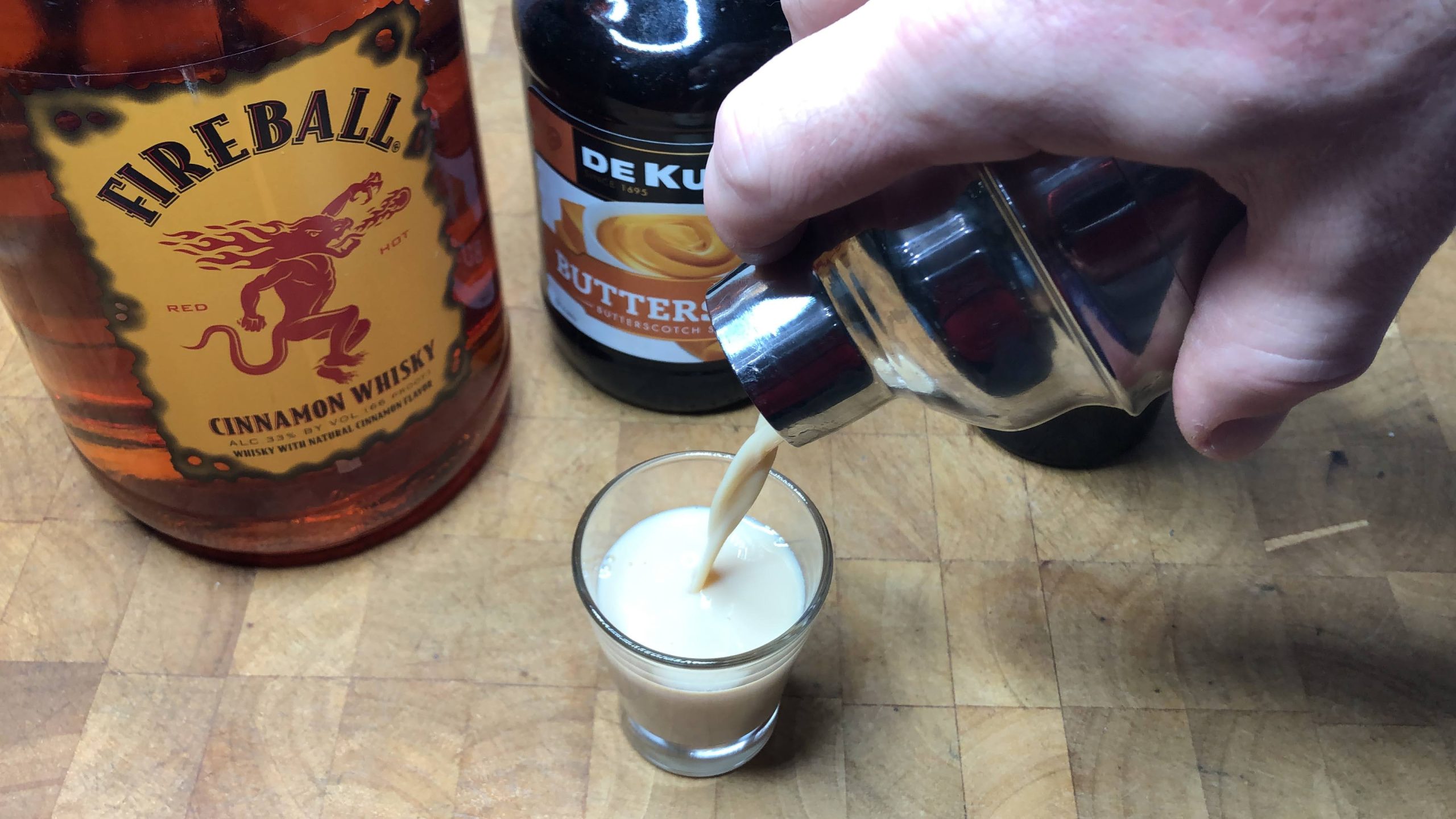 Pouring oatmeal cookie shot from a shaker into a shot glass.