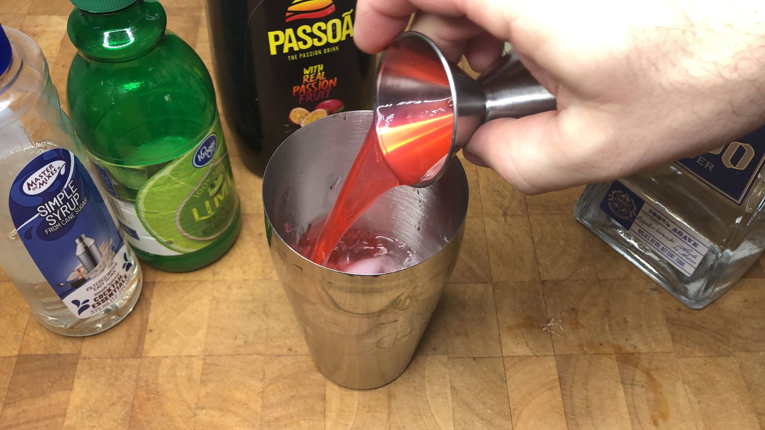 Pouring passion fruit liqueur from a jigger into the shaker.