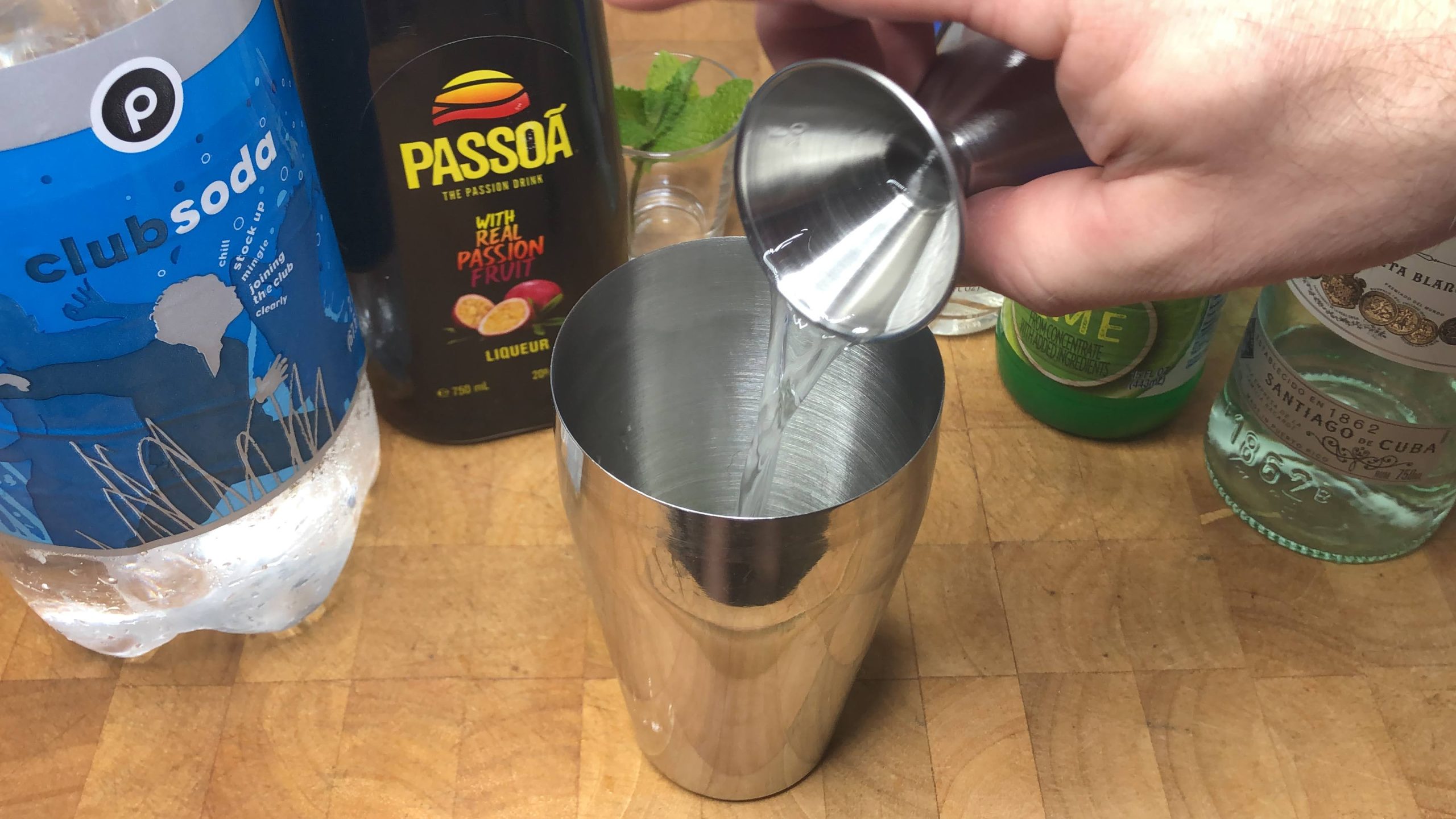 Pouring white rum from a jigger into a shaker.