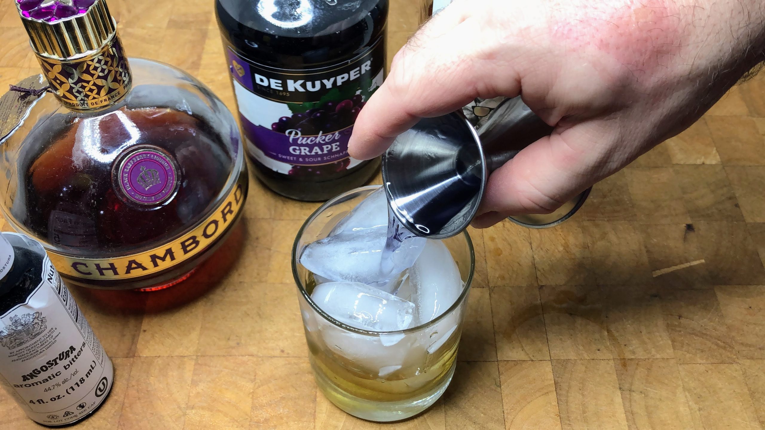 Pouring grape pucker from jigger into glass.