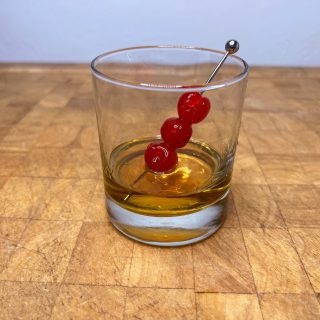 Closeup of a Peanut Butter Whiskey Old fashioned in a rocks glass with three maraschino cherries.