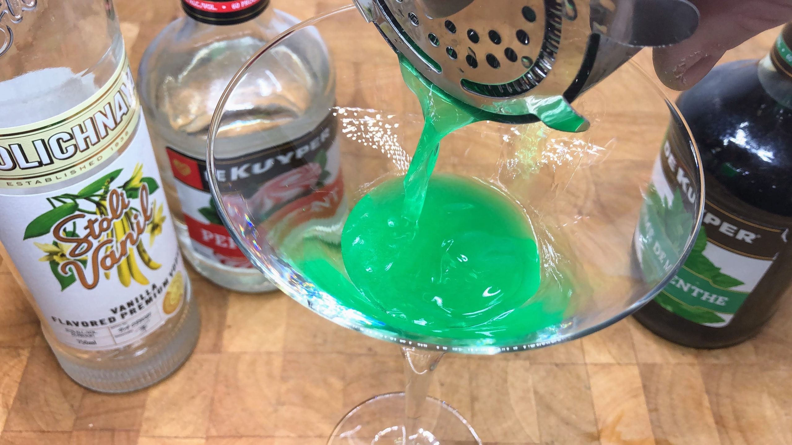 Pouring peppermint martini from a shaker into a martini glass.