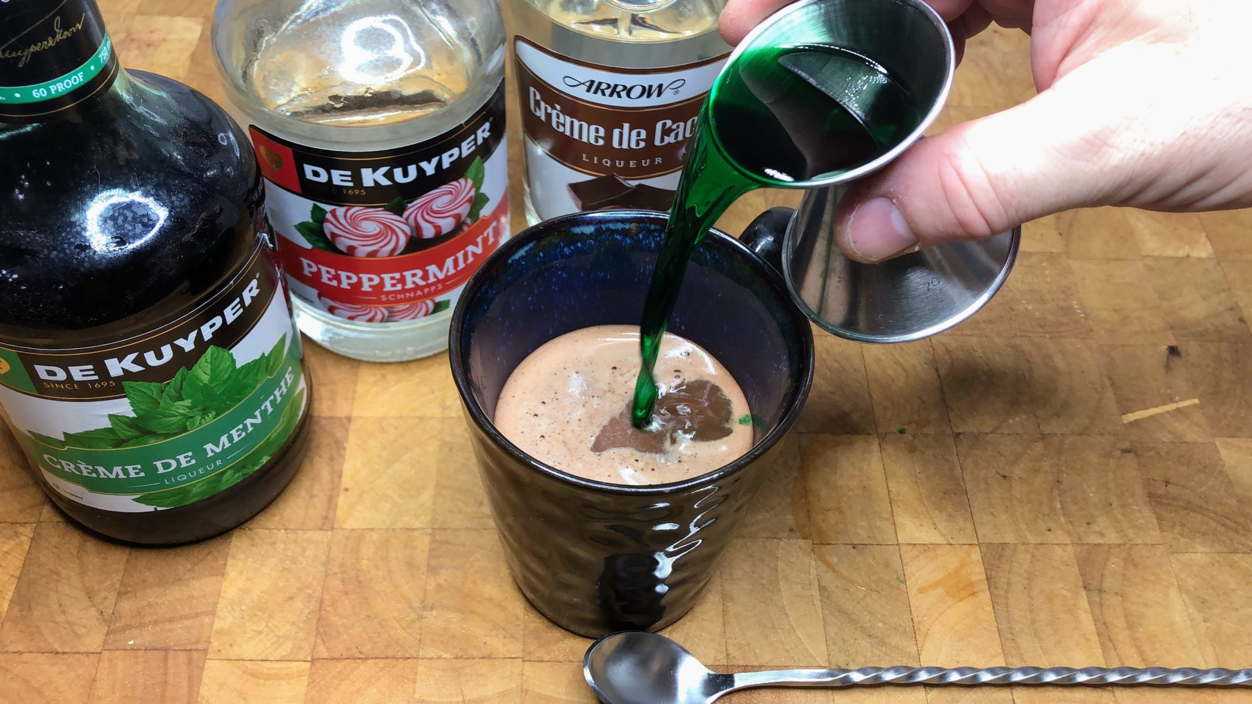 Adding creme de menthe into a mug.