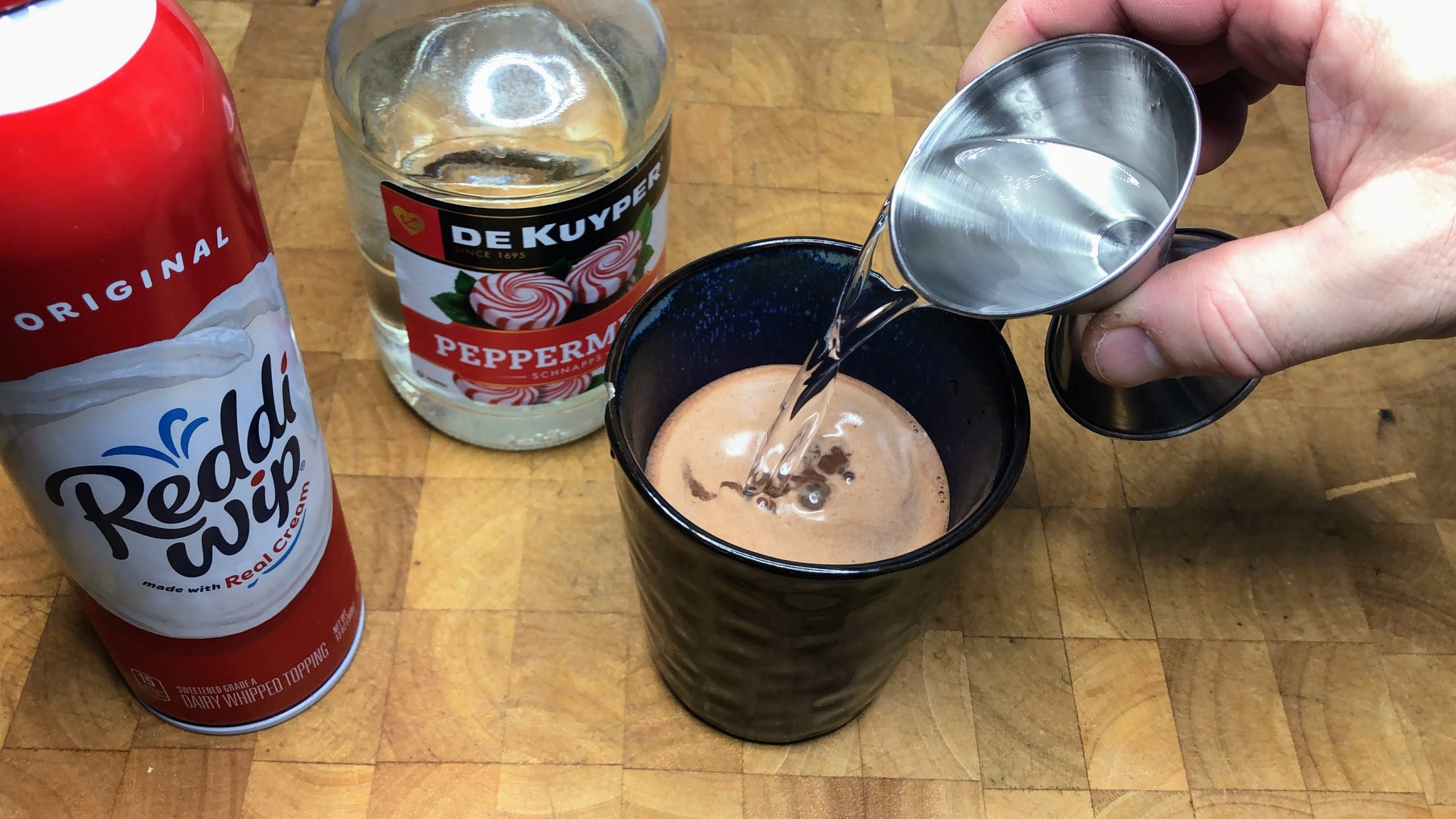 Pouring peppermint schnapps into a mug.