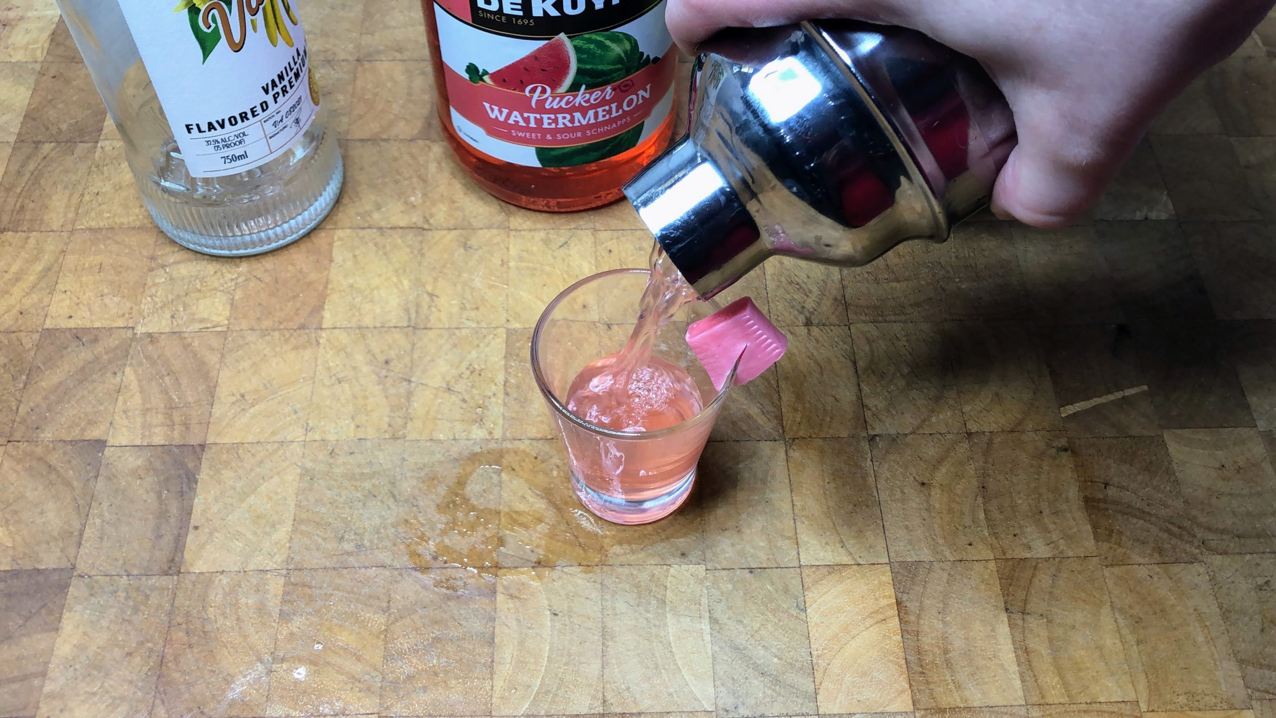 Pouring pink starburst shot from shaker into shot glass.